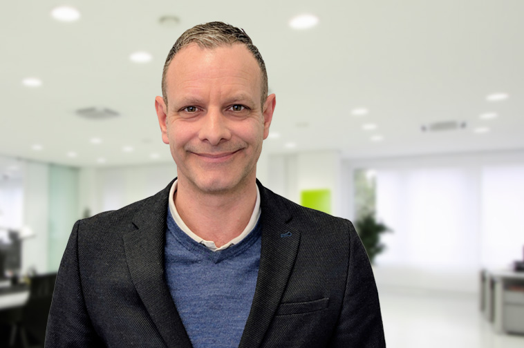 Nick Lowe standing in front of a blurred office background